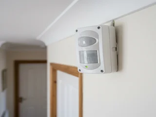 Dual-technology PIR and microwave motion detector mounted on a wall in a commercial Singapore installation